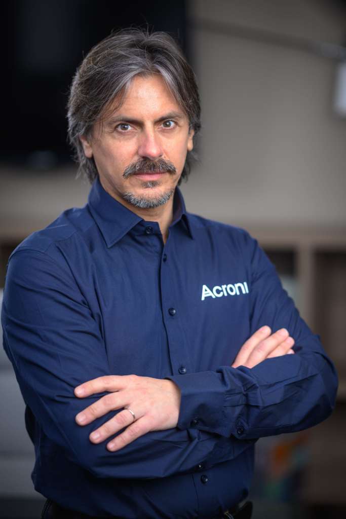 Denis Cassinerio in posa, indossa una camicia blu con logo Acronis